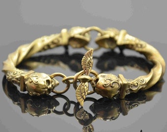 May include: A gold-toned bracelet with a twisted design and skull-shaped accents. The bracelet features a winged charm in the center.