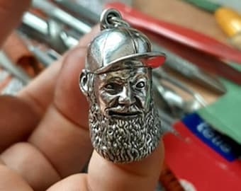May include: A silver charm of a man with a beard wearing a baseball cap. The charm is detailed and has a realistic look.