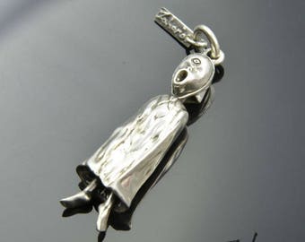May include: A silver pendant in the shape of a stylized figure with an open mouth and flowing robe. The pendant has a loop for a chain and the word "Zahario" is visible on the pendant.