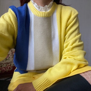 May include: A yellow, blue and white striped sweater with a crew neck.