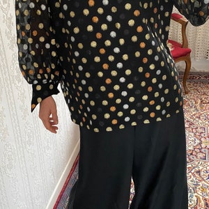 May include: A black sheer blouse with gold, silver, and copper polka dots. The blouse has long sleeves and a round neckline.