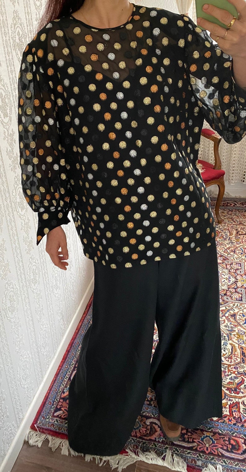 May include: A black sheer blouse with gold, silver, and copper polka dots. The blouse has long sleeves and a round neckline.