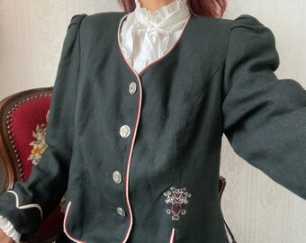 May include: A black jacket with red and white trim, silver buttons, and embroidery. The jacket has a round neckline and long sleeves with puffed shoulders. A white blouse with a ruffled collar is visible underneath.