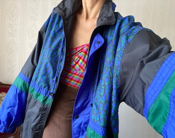 May include: A vintage windbreaker jacket in blue, black, and green. The jacket features a blue and green patterned design on the front and a black collar. The sleeves are blue and black with green stripes. A colorful plaid top is visible underneath.