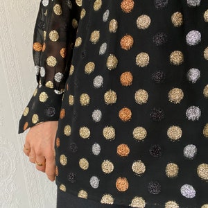 May include: Black sheer blouse with long sleeves and a polka dot pattern. The dots are made of gold, silver, and copper glitter.