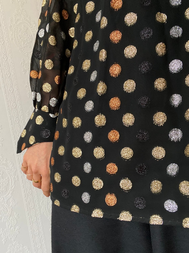 May include: Black sheer blouse with long sleeves and a polka dot pattern. The dots are made of gold, silver, and copper glitter.