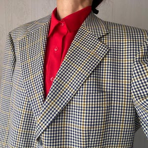 May include: A checkered blazer with a white, blue, and brown pattern. The blazer has a red collared shirt underneath.