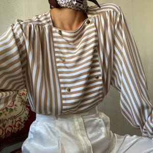 May include: A brown and white striped long-sleeve blouse with a button-up front and a white collar. The blouse has a relaxed fit and is made of a soft, silky fabric.