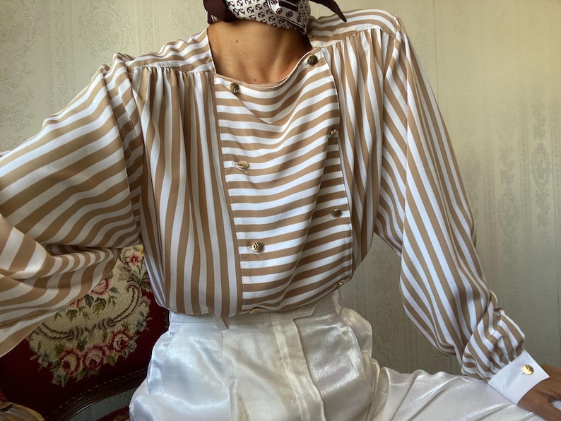 May include: A brown and white striped long-sleeve blouse with a button-up front and a white collar. The blouse has a relaxed fit and is made of a soft, silky fabric.