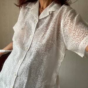 May include: White sheer button-up shirt with a floral pattern.