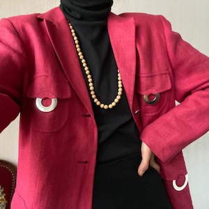 May include: A pink linen blazer with two large silver rings on the pockets and a wooden bead necklace.