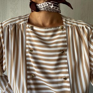 May include: A brown and white striped blouse with a button-up front and long sleeves. The blouse has a square neckline and a relaxed fit.