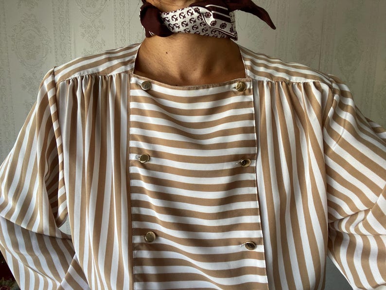 May include: A brown and white striped blouse with a button-up front and long sleeves. The blouse has a square neckline and a relaxed fit.