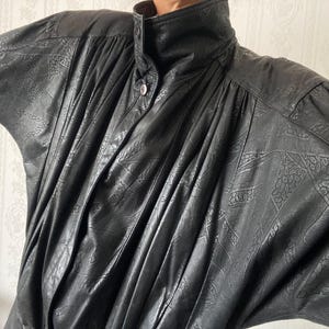 Op de afbeelding: Zwarte leren jas met een hoge kraag en knoopsluiting. De jas heeft een gestructureerd, patroonontwerp en lange mouwen. Het kledingstuk heeft een vintage esthetiek en een relaxte pasvorm, geschikt voor diverse gelegenheden.