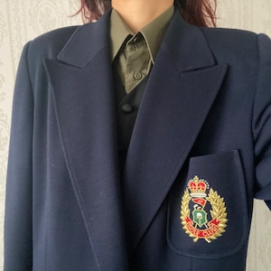 Könnte beinhalten: Ein marineblauer Blazer mit einem goldenen gestickten Aufnäher, auf dem "Golf Club" steht und eine Krone, einen Golfschläger und einen Golfball abgebildet sind.