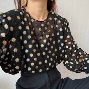 May include: A black sheer blouse with gold, silver, and copper polka dots. The blouse has long sleeves with a gathered detail at the shoulders.