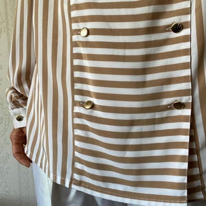 May include: A brown and white striped long-sleeve shirt with gold buttons. The shirt has a double-breasted closure.