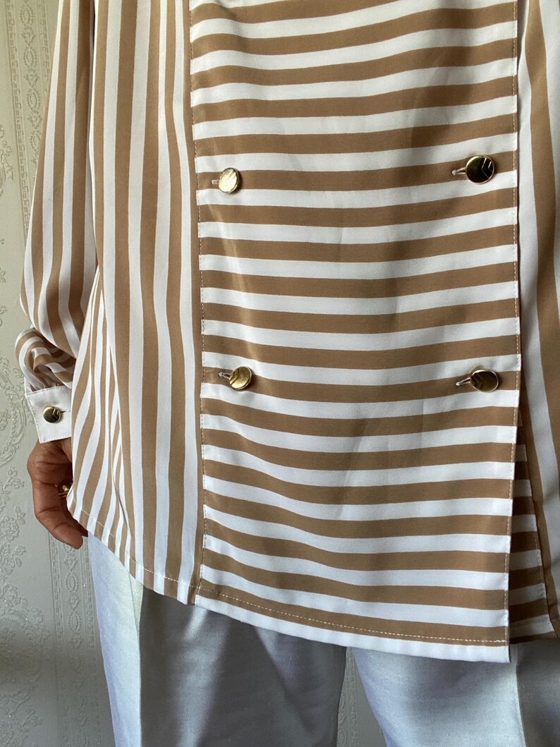 May include: A brown and white striped long-sleeve shirt with gold buttons. The shirt has a double-breasted closure.