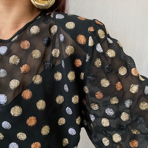May include: A black sheer blouse with gold, silver, and copper polka dots.