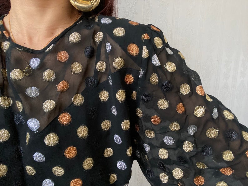 May include: A black sheer blouse with gold, silver, and copper polka dots.