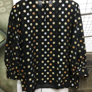 May include: A black sheer blouse with a round neckline and long sleeves. The blouse is covered in a polka dot pattern with gold, silver, and copper colored dots.