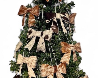 Puede incluir: Una colección de adornos decorativos en forma de lazo hechos de piel de vaca texturizada en varios tonos de marrón, beige, negro y blanco. Cada lazo presenta un patrón de estampado animal único y está suspendido por un hilo fino.