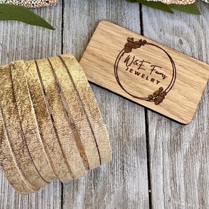 May include: A close-up of a stack of beige leather strips with a distressed finish. The leather is arranged in a circular pattern. A wooden sign with the text "W&E Famy Jewelry" is visible in the background.