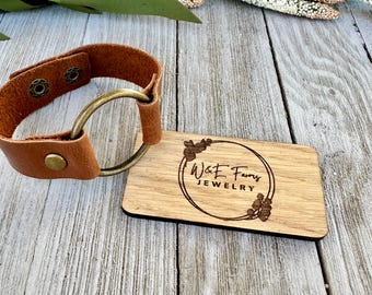 May include: A brown leather bracelet with a brass ring and two brass snaps. The bracelet is on a wooden surface with a business card that says "W&E Farms Jewelry".