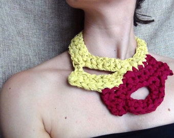 May include: A yellow and red crocheted necklace. The necklace is made of two different types of yarn, one yellow and one red. The necklace is worn by a person with fair skin.