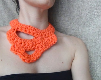 May include: A bright orange crocheted necklace with a large, open design. The necklace is made of thick yarn and has a chunky, textured look.