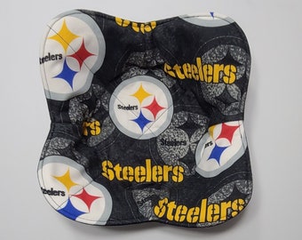 May include: A quilted, padded oven mitt featuring a repeating pattern of the Pittsburgh Steelers logo in black, yellow, red, and blue. The word "Steelers" is printed in yellow on the mitt.