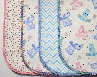 May include: A selection of baby blankets with diverse patterns and colours. The blankets display designs such as polka dots, a blue and white chevron pattern, and a repeating pattern of pastel cartoon animals. Each blanket has a crocheted edge.