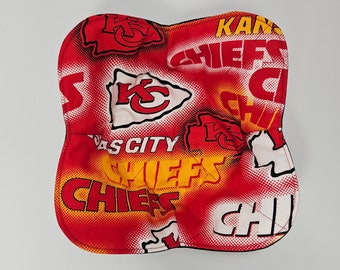 May include: A red and white Kansas City Chiefs themed square fabric item. The fabric features the Chiefs logo, the words "Kansas City" and "Chiefs" in a repeating pattern. The item has a black border.