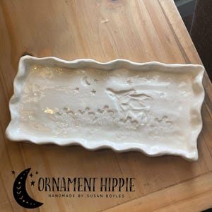 May include: White ceramic tray with a wavy edge. The tray has a raised design of a flying witch with stars and a crescent moon.