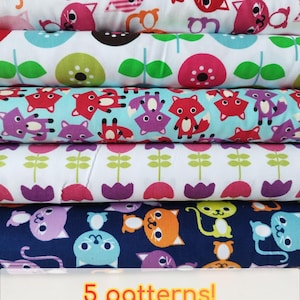 Puede incluir: Una pila de rollos de tela con varios patrones coloridos. Los diseños incluyen gatos, zorros y motivos florales en tonos de rojo, azul, morado y verde. El texto "5 patterns!" es visible en la parte inferior.