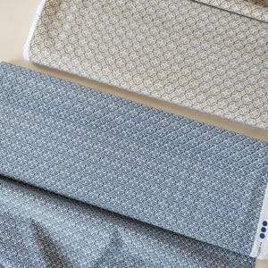 May include: Two folded bolts of fabric featuring a repeating geometric pattern of interlocking circles and diamonds. One bolt is in shades of beige and dark brown, while the other is in navy blue and white, with a small white selvage edge visible.