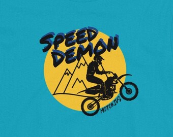 May include: A turquoise blue youth t-shirt with a graphic of a person riding a dirt bike in front of mountains. The graphic is surrounded by a yellow circle with the text "SPEED DEMON MOTORSPORTS" in blue and black lettering.