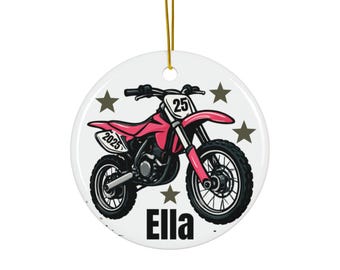 May include: A white ceramic ornament featuring a pink dirt bike with black tires and the number 25. The ornament includes the name "Ella" and the year "2025". Gold string for hanging.
