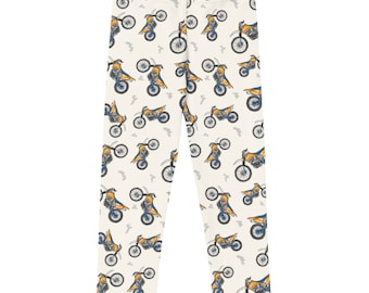 May include: White leggings with a repeating pattern of yellow and blue dirt bikes. The bikes are drawn in a cartoon style.