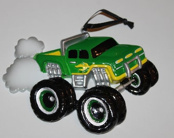 May include: Green monster truck Christmas ornament with white smoke coming out of the exhaust pipe. The truck has a yellow flame design on the side and black wheels.