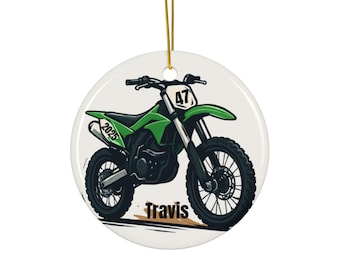 May include: A round ceramic ornament featuring a green and black motocross bike. The bike has the number 47 on the front and the year 2025 on the side. The name "Travis" is printed below the bike.
