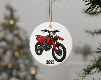 May include: White ceramic ornament featuring a red and black dirt bike illustration. The bike has the number 96 on the front and the year 2025 below. The ornament hangs from a gold string.