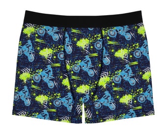 May include: Boxer briefs with a navy blue background and a pattern of blue motocross riders, green paint splatters, and white geometric shapes. The waistband is black.