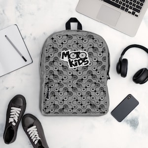 May include: Gray backpack with a black and white chain pattern and a black logo that says "Moto Kids".