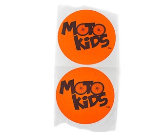 May include: Two orange round stickers with the text "Moto Kids" in black lettering and a black bicycle wheel graphic. The text "TM" is in smaller black lettering below the word "Kids".