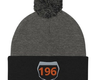 May include: Gray and black knit beanie with a pom pom on top. The beanie has a gray top and a black bottom with a white and gray highway sign with the number 196 in orange.