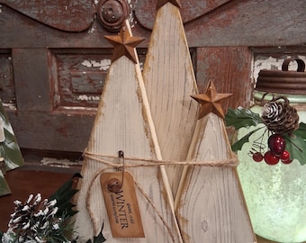 May include: Three wooden Christmas tree decorations. Each tree is painted white with a rustic finish and topped with a rusty star. The trees are tied together with twine and a tag that reads "Winter".