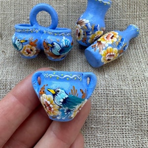 Op de afbeelding: Een verzameling miniatuur lichtblauwe keramische vaten met handgeschilderde gele bloemen en blauwe vogels. De set bevat een pot met twee oren, een klein vaasje, een fles en een pot met één oor, allemaal versierd met witte stippen.