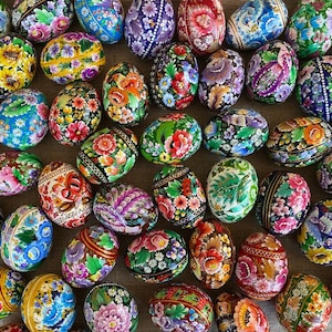 Puede incluir: Una colección de huevos de Pascua pintados de forma intrincada con diseños florales y geométricos en colores vibrantes, incluyendo rojo, azul, verde, amarillo y blanco.