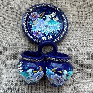 Peut inclure: Un ensemble en céramique bleu foncé composé d'une assiette décorative ronde et d'un récipient à deux compartiments avec une anse centrale. Les deux pièces présentent des oiseaux bleu clair, des fleurs violettes et blanches et des dorures.